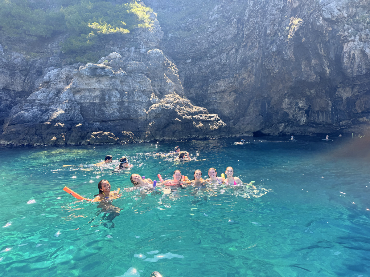 Group swimming with pool noodles in turquoise water at a swim stop on a Dubrovnik Blue Cave tour