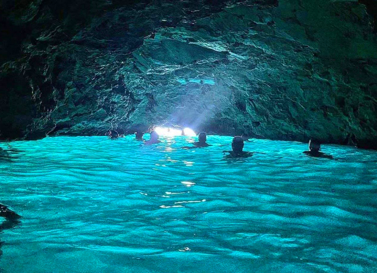Swimmers inside the Blue Cave with glowing turquoise water lit from below, near Dubrovnik
